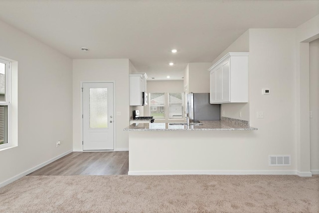 kitchen with stainless steel refrigerator, white cabinetry, light stone counters, light colored carpet, and kitchen peninsula