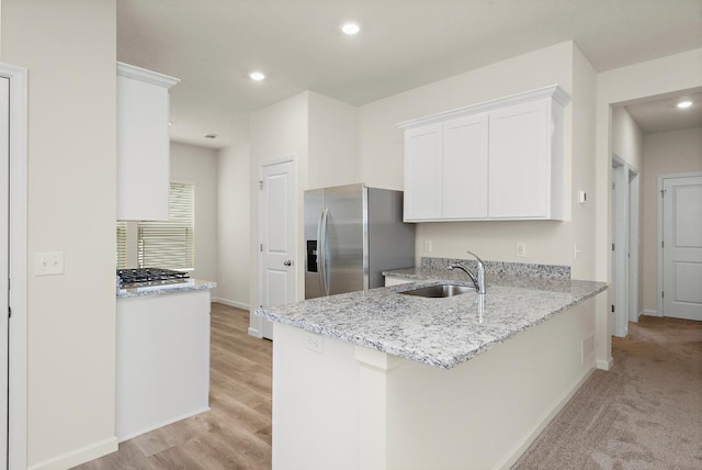 kitchen with sink, white cabinets, stainless steel fridge, light stone counters, and kitchen peninsula