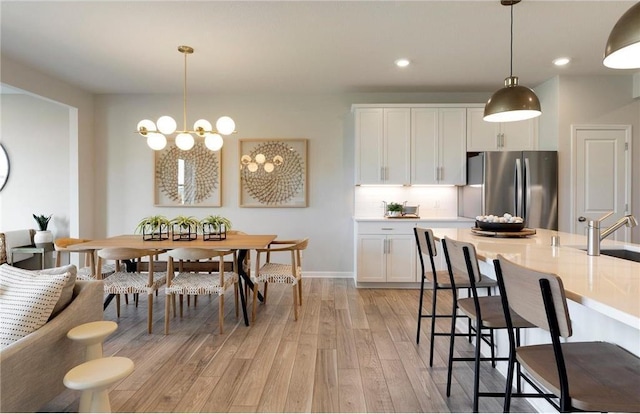 kitchen featuring white cabinetry, light hardwood / wood-style flooring, stainless steel fridge, pendant lighting, and backsplash