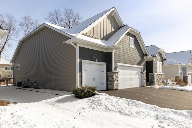 snow covered property with an attached garage and central air condition unit