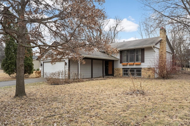 tri-level home featuring aphalt driveway, brick siding, a chimney, and an attached garage