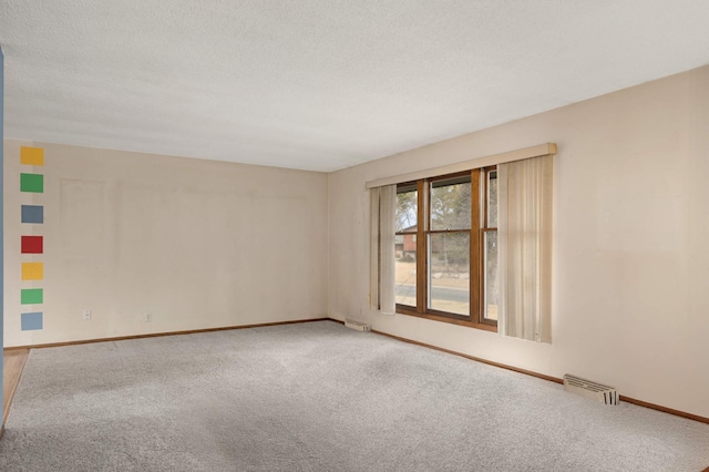 carpeted empty room with visible vents, a textured ceiling, and baseboards