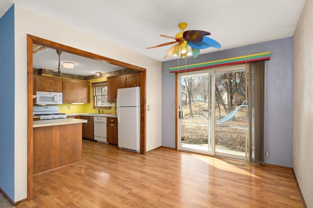 kitchen with light wood finished floors, light countertops, white appliances, and a healthy amount of sunlight