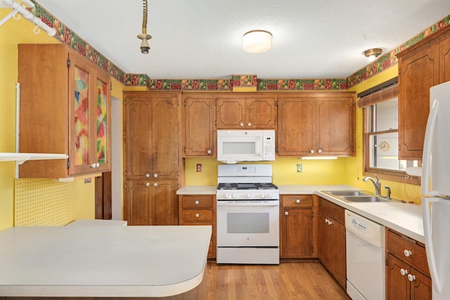 kitchen featuring brown cabinetry, white appliances, and a sink