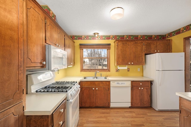 kitchen with brown cabinetry, white appliances, a sink, and light wood-style flooring