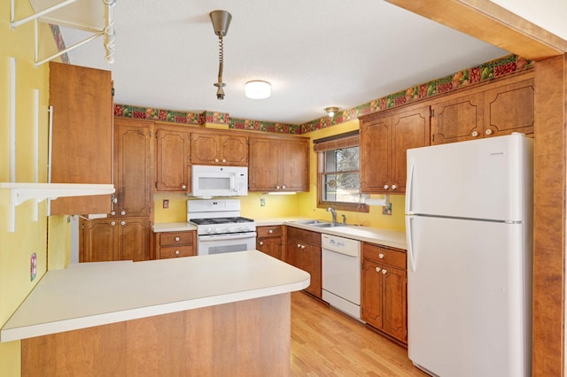 kitchen featuring brown cabinetry, light wood-style floors, a sink, white appliances, and a peninsula