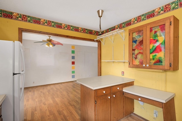 kitchen featuring a peninsula, light countertops, freestanding refrigerator, light wood finished floors, and brown cabinetry