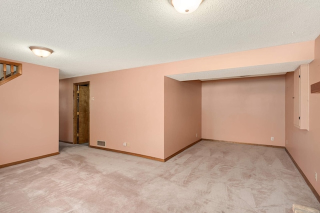 finished below grade area featuring light carpet, visible vents, baseboards, and a textured ceiling