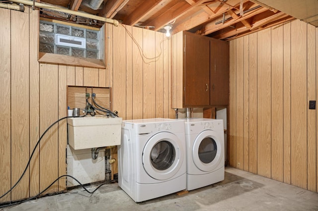 washroom featuring laundry area, washing machine and dryer, wooden walls, and a sink