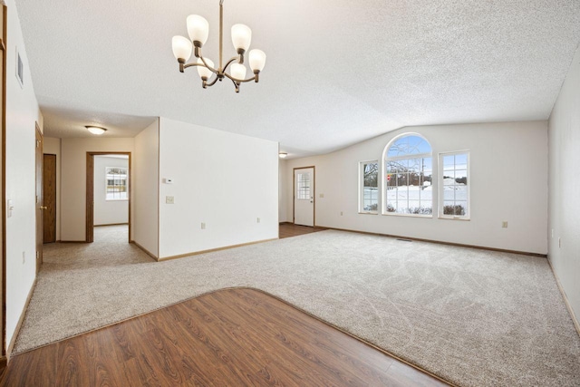 carpeted spare room with lofted ceiling, a healthy amount of sunlight, a notable chandelier, and a textured ceiling