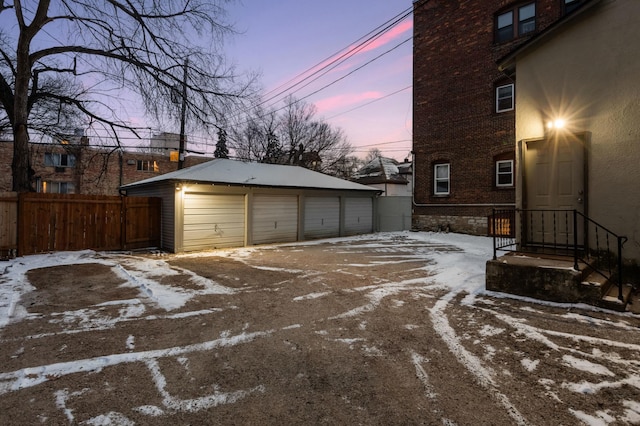 snow covered garage featuring a detached garage and fence