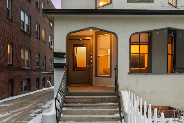 snow covered property entrance with fence and stucco siding