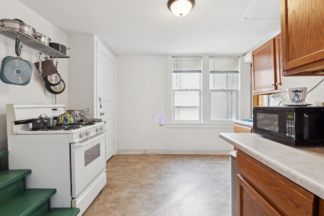 kitchen featuring baseboards, black microwave, white gas stove, light countertops, and brown cabinetry