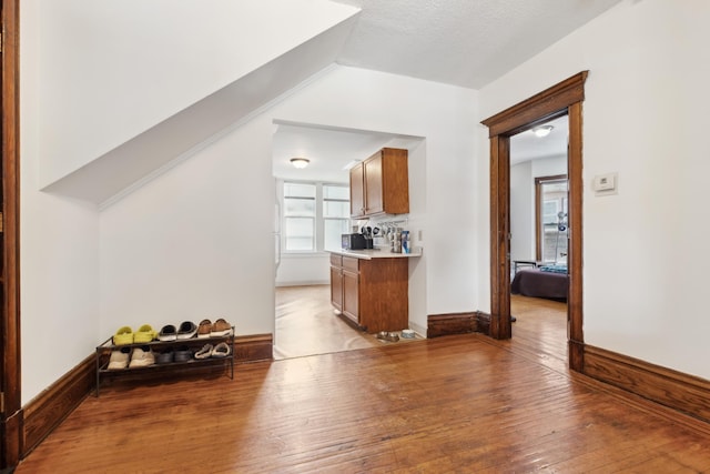 interior space with brown cabinetry, light wood-type flooring, a textured ceiling, light countertops, and baseboards