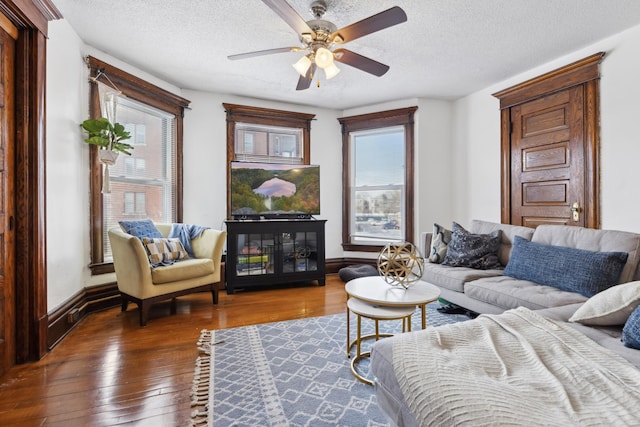 living area featuring a textured ceiling, wood-type flooring, a ceiling fan, and baseboards