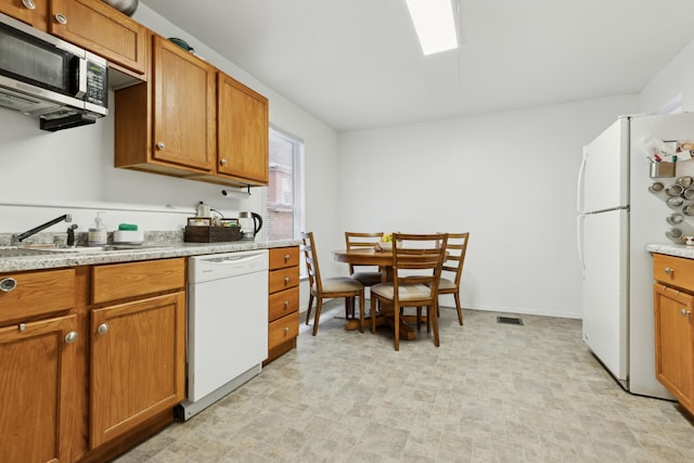kitchen featuring baseboards, white appliances, visible vents, brown cabinetry, and a sink