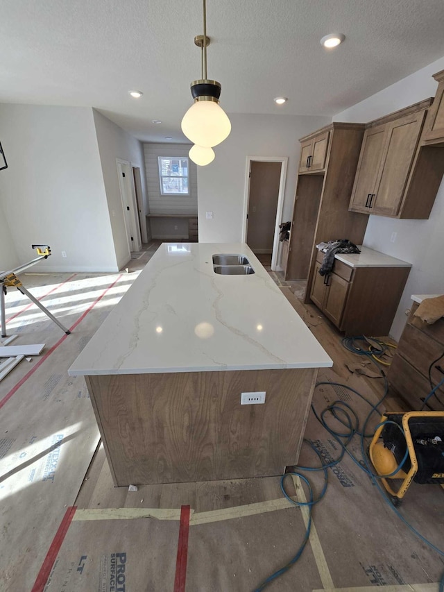 kitchen with a textured ceiling, a kitchen island, light stone countertops, and hanging light fixtures