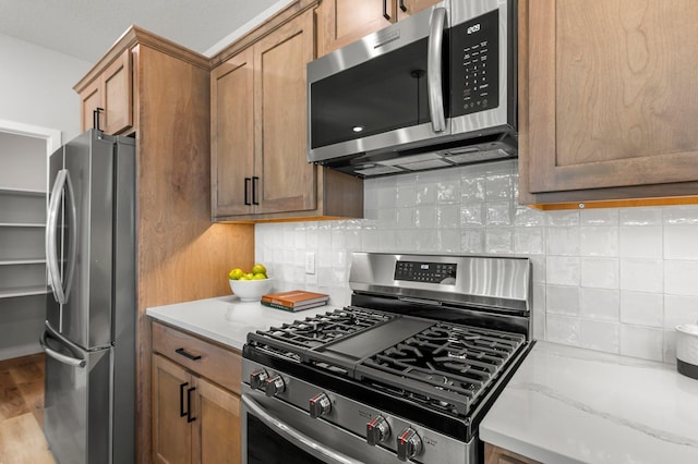 932 Orchard Ln, Roseville, MN 55113 - kitchen featuring stainless steel appliances, backsplash, light stone countertops, brown cabinetry, and wood finished floors