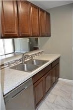 kitchen featuring light countertops, stainless steel dishwasher, a sink, and baseboards