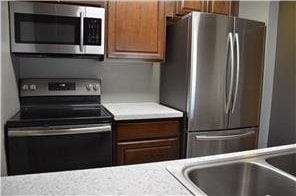 kitchen featuring brown cabinetry, appliances with stainless steel finishes, light countertops, and a sink