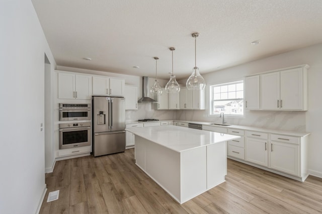 kitchen with appliances with stainless steel finishes, white cabinetry, a center island, decorative light fixtures, and wall chimney exhaust hood