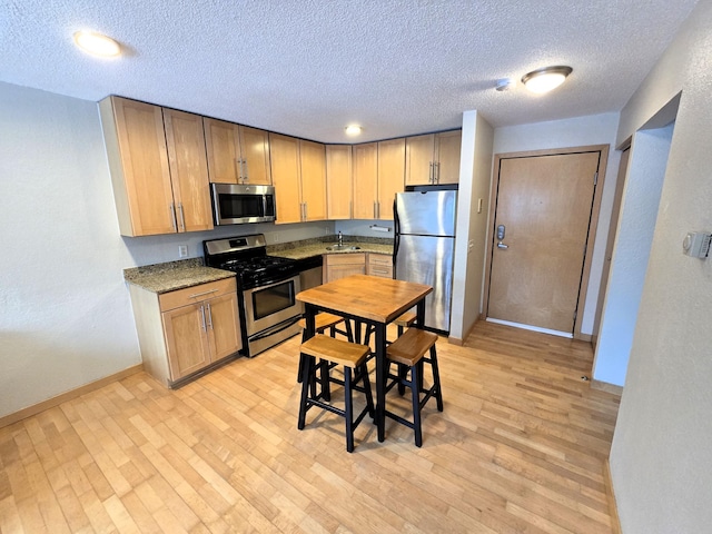 kitchen with sink, a textured ceiling, stainless steel appliances, light stone countertops, and light hardwood / wood-style floors