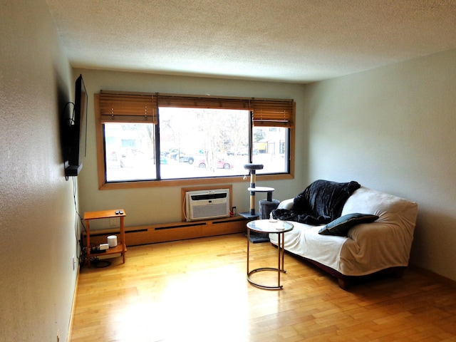 sitting room featuring a wall mounted air conditioner, a textured ceiling, light hardwood / wood-style flooring, and a baseboard radiator