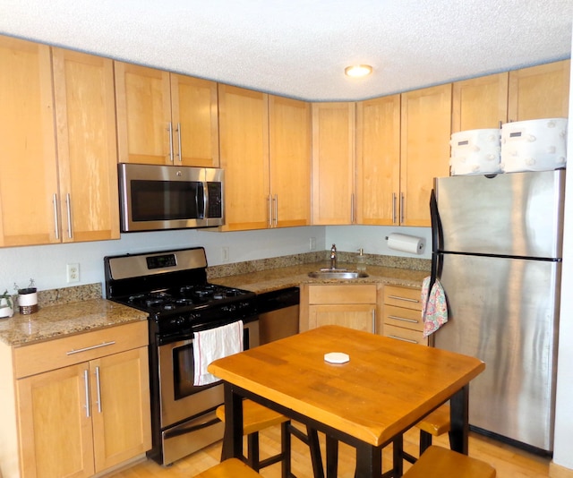 kitchen featuring appliances with stainless steel finishes, light stone countertops, sink, and a textured ceiling