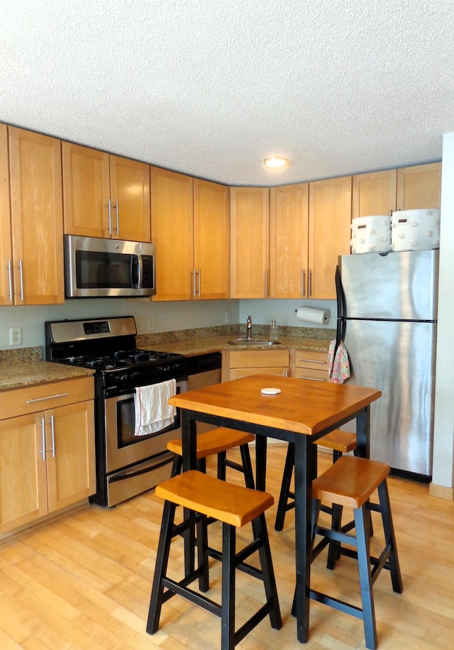 kitchen featuring sink, light wood-type flooring, light stone countertops, and appliances with stainless steel finishes