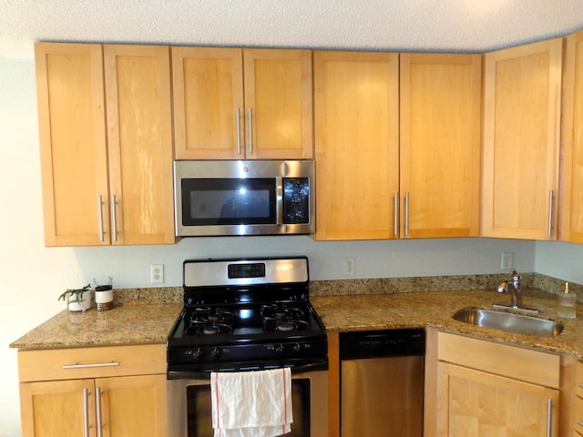 kitchen with stainless steel appliances, light stone countertops, and sink