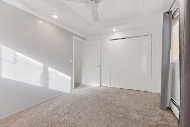 unfurnished bedroom with crown molding, light carpet, a raised ceiling, a closet, and a baseboard heating unit