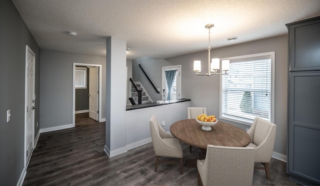 dining room with dark wood-type flooring, a textured ceiling, stairway, an inviting chandelier, and baseboards