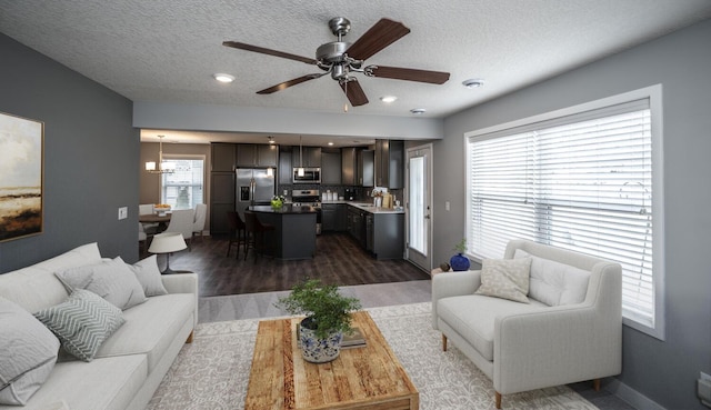 living room with a textured ceiling, dark wood-type flooring, baseboards, and ceiling fan