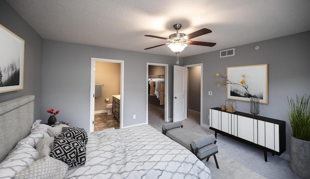 bedroom with a spacious closet, visible vents, carpet, a textured ceiling, and a ceiling fan