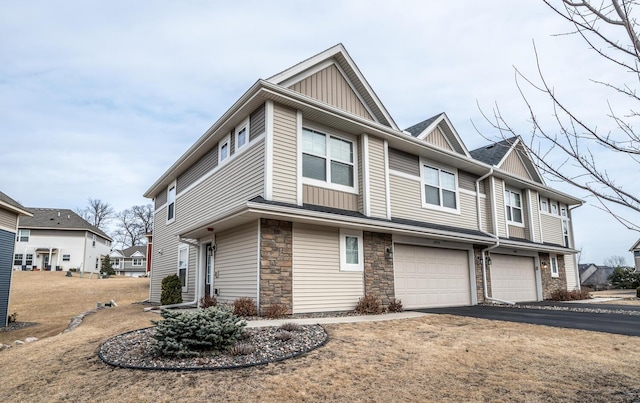 view of property featuring stone siding, board and batten siding, an attached garage, and driveway