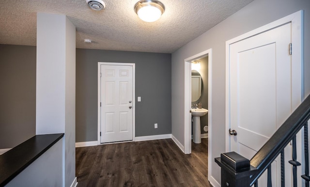 hall featuring dark wood finished floors, a textured ceiling, baseboards, and a sink