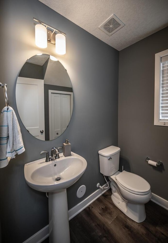 half bathroom with toilet, wood finished floors, visible vents, and baseboards