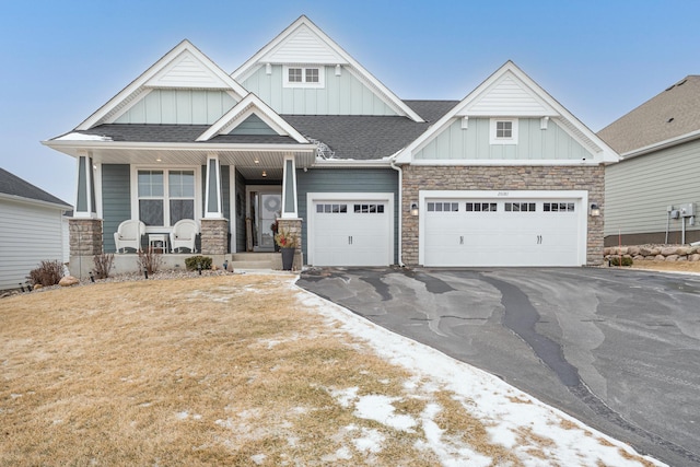 craftsman house featuring covered porch, driveway, stone siding, roof with shingles, and board and batten siding