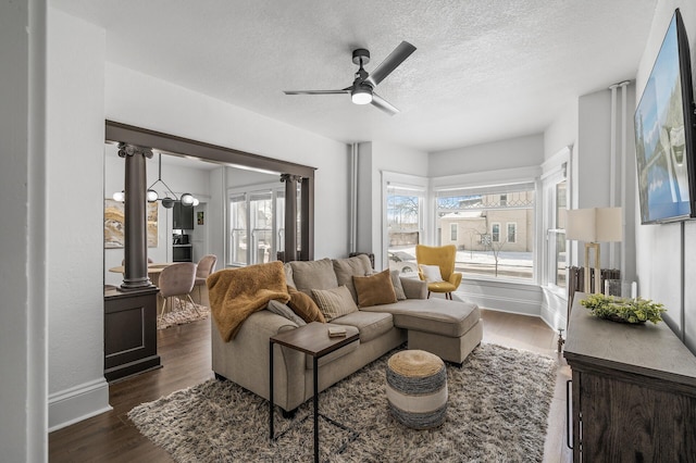 living room featuring ceiling fan, dark wood-type flooring, decorative columns, and a textured ceiling