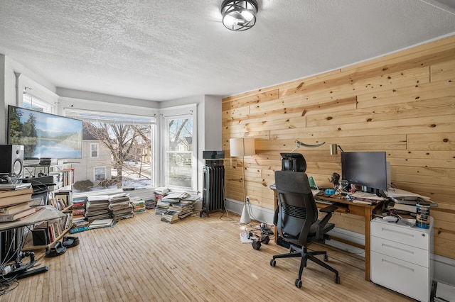 home office featuring a healthy amount of sunlight, a textured ceiling, light hardwood / wood-style flooring, and wood walls