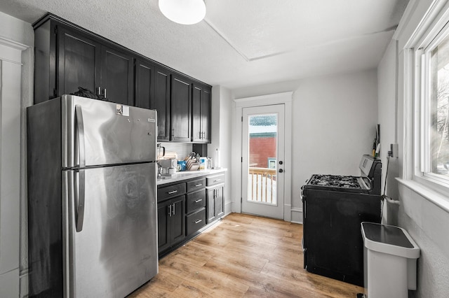 kitchen featuring washer / dryer, range with gas cooktop, a textured ceiling, stainless steel refrigerator, and light hardwood / wood-style floors