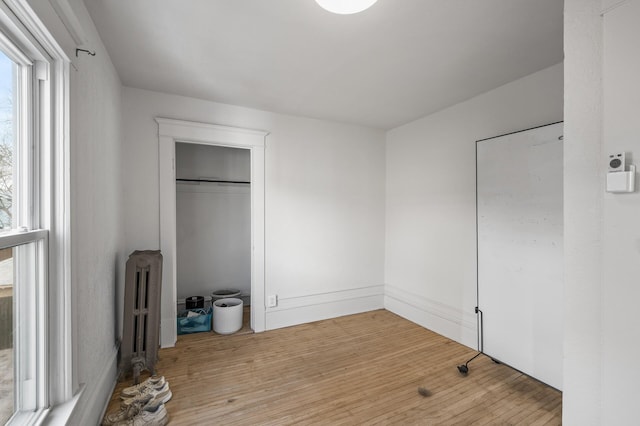 unfurnished bedroom with radiator heating unit, light hardwood / wood-style floors, and a closet