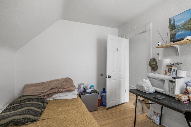 bedroom featuring vaulted ceiling, a textured ceiling, and light hardwood / wood-style floors