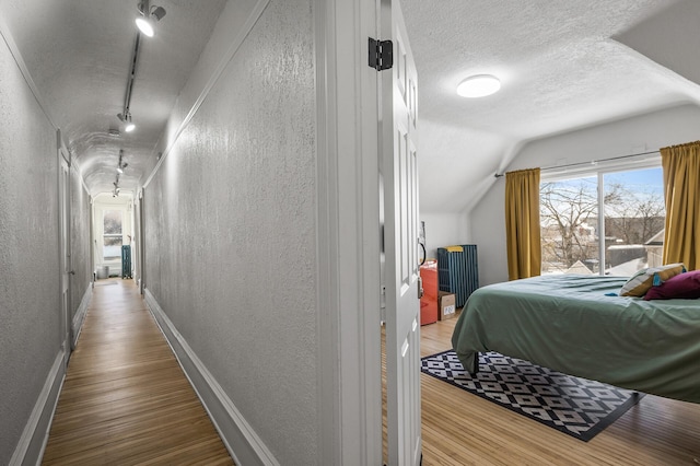 bedroom with lofted ceiling, hardwood / wood-style floors, track lighting, and a textured ceiling