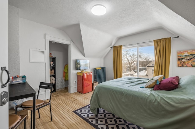 bedroom with vaulted ceiling, a textured ceiling, and light hardwood / wood-style floors