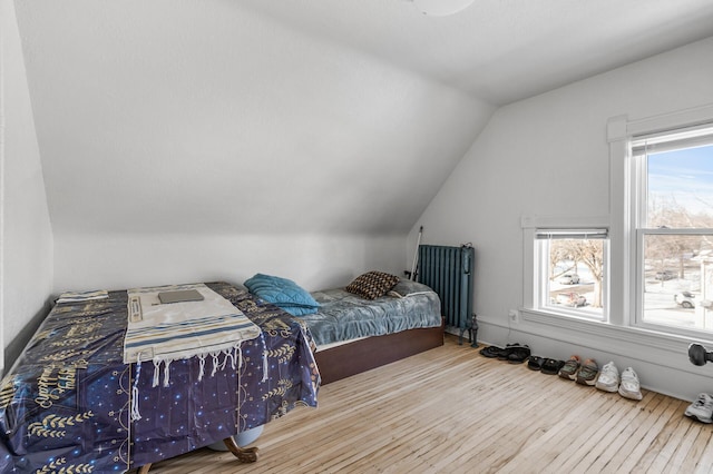 bedroom with hardwood / wood-style floors, vaulted ceiling, and radiator heating unit