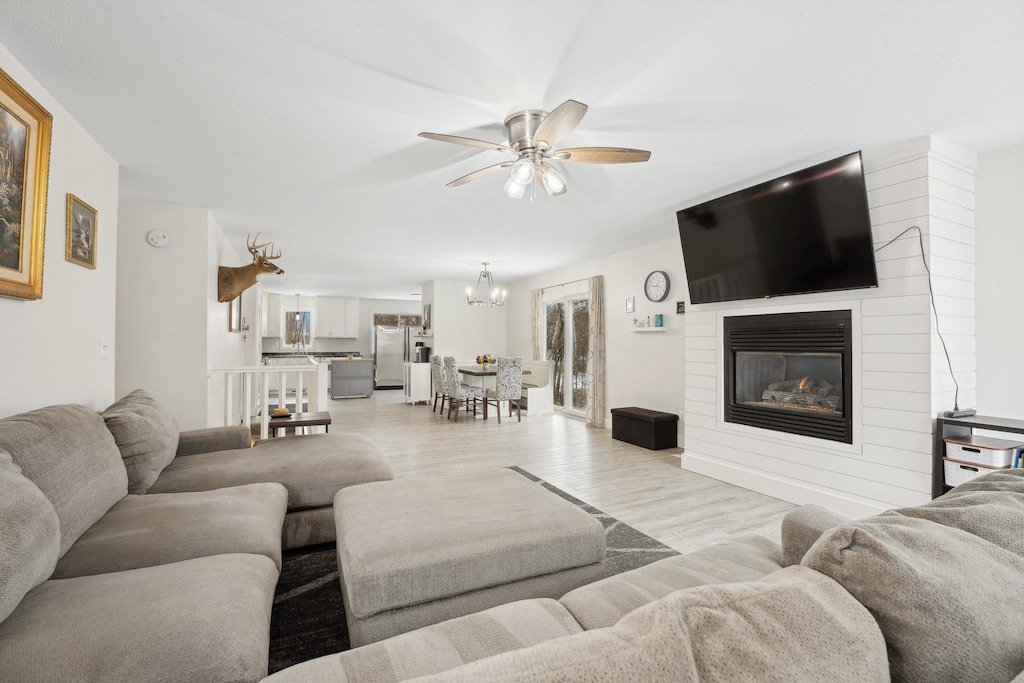 living room featuring light wood-type flooring, a large fireplace, and ceiling fan with notable chandelier