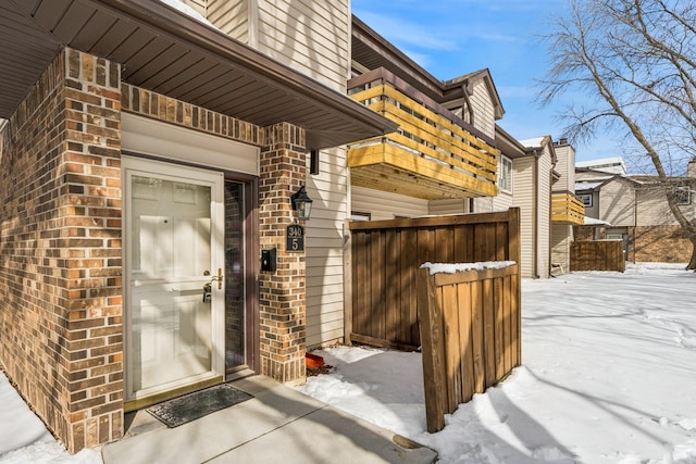 snow covered property entrance featuring brick siding and fence