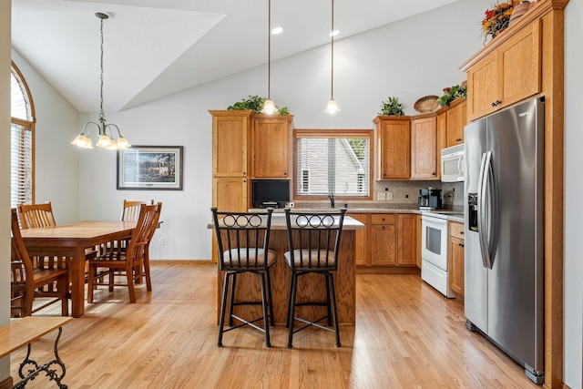 kitchen with white appliances, a breakfast bar area, hanging light fixtures, a center island, and light wood-type flooring