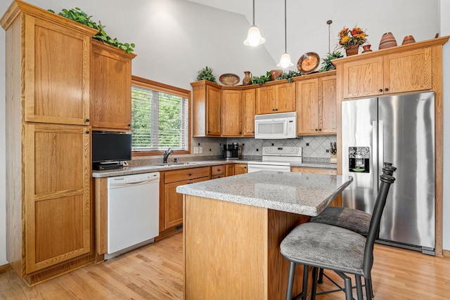 kitchen featuring a kitchen island, decorative light fixtures, sink, light stone countertops, and white appliances